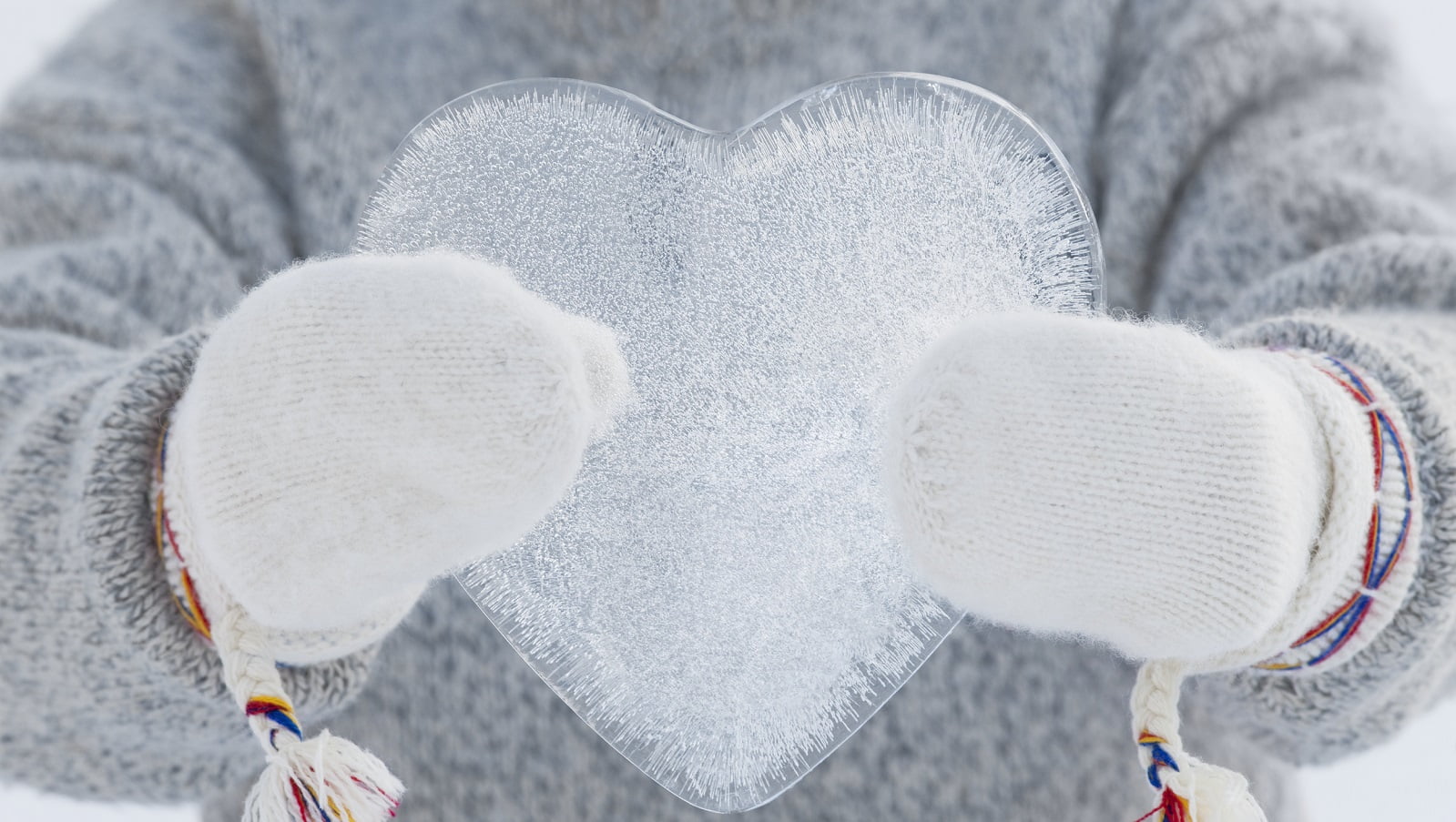 To hvite strikkevotter holder en isbit formet som et hjerte