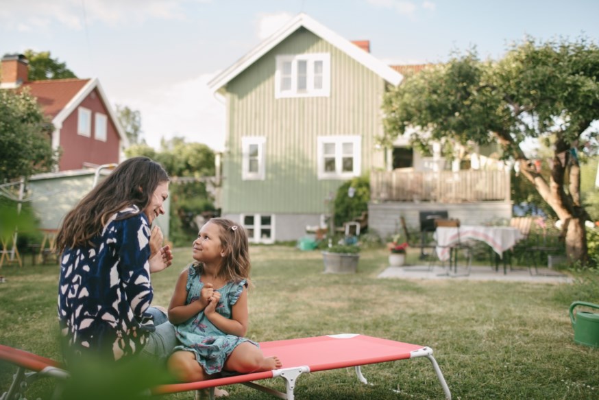 Mor og datter sitter på en solseng i en hage utenfor en hus